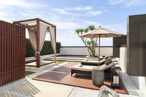 A modern outdoor lounge area with a wooden pergola, a cushioned seating area, and a decorative planter.