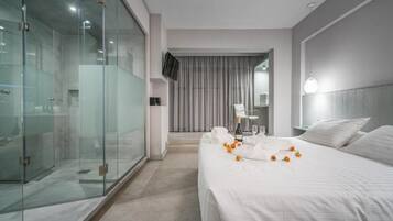 A hotel room with a bed, a glass shower enclosure, a television, and a view of the street.