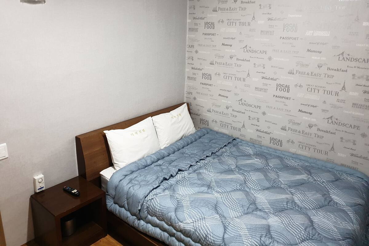 Un dormitorio con una cama, una mesita de noche y una pared con palabras relacionadas con viajes.