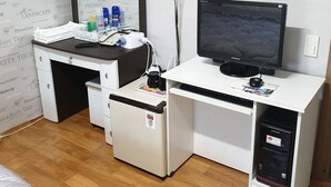 Una habitación con escritorio, dos monitores, un refrigerador y una cama.