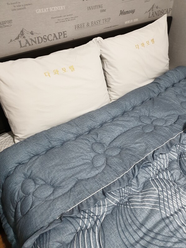 Una cama con una colcha azul estampada y almohadas blancas con texto coreano.
