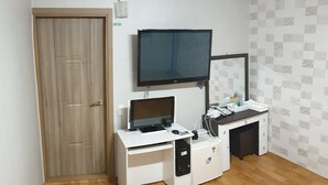 Una habitación con una puerta de madera, un escritorio blanco con un ordenador, un monitor y un refrigerador pequeño.