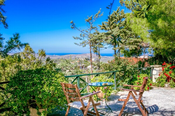 A patio with two wooden chairs and a small round table, overlooking a scenic landscape with trees and a distant view of the sea. - Agapi Villa (Hersonissos)
