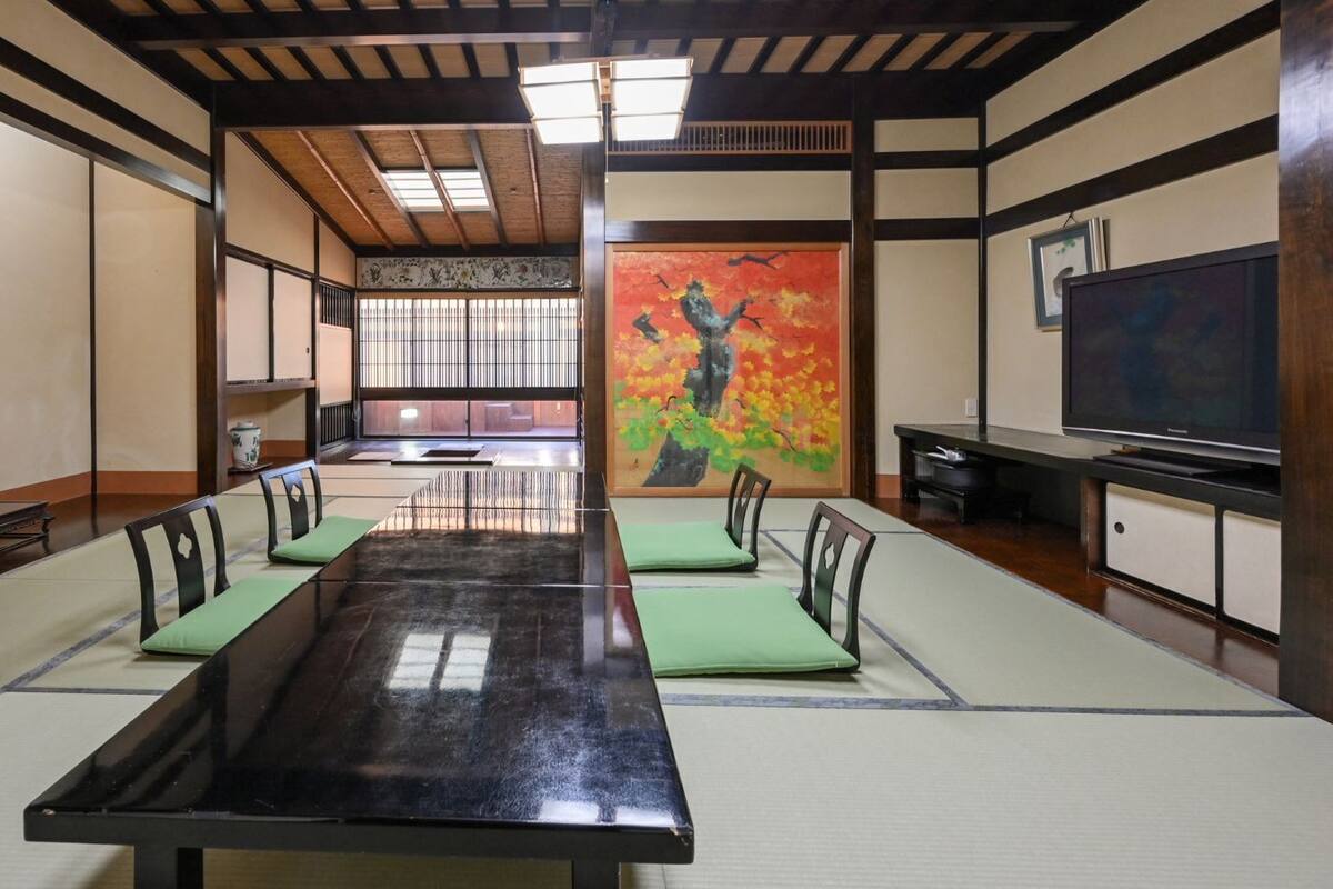 Una habitación tradicional con tatami, una mesa de tatami, cojines verdes, una pintura y un televisor.