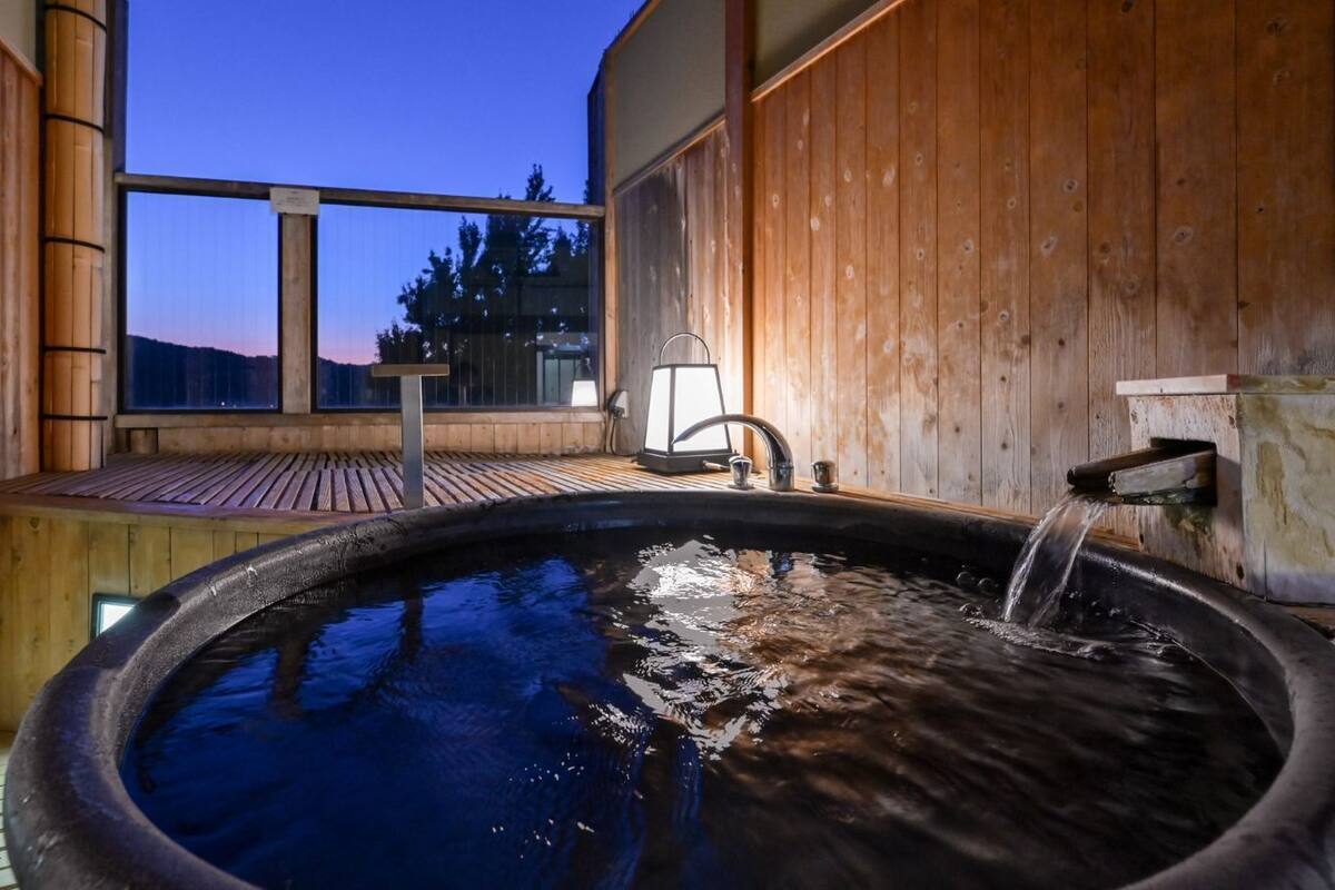 Un spa de madera con hidromasaje, terraza de madera y vistas a la montaña.