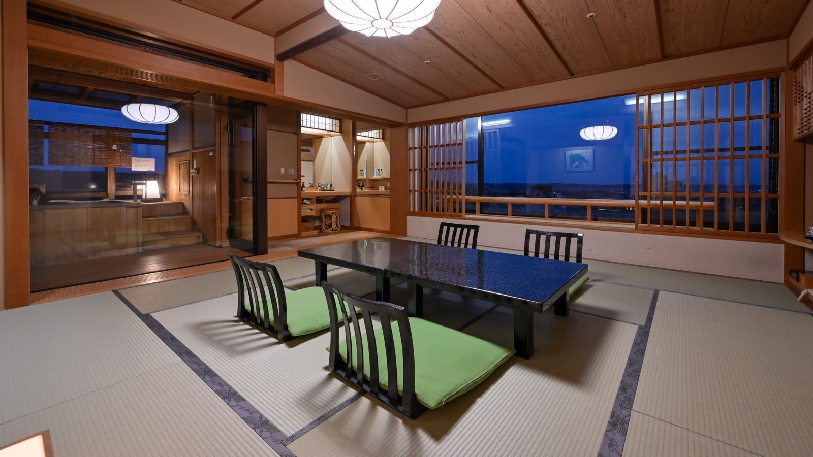 A tatami mat room with a low table and chairs, wooden sliding doors, and a view through a shoji screen.