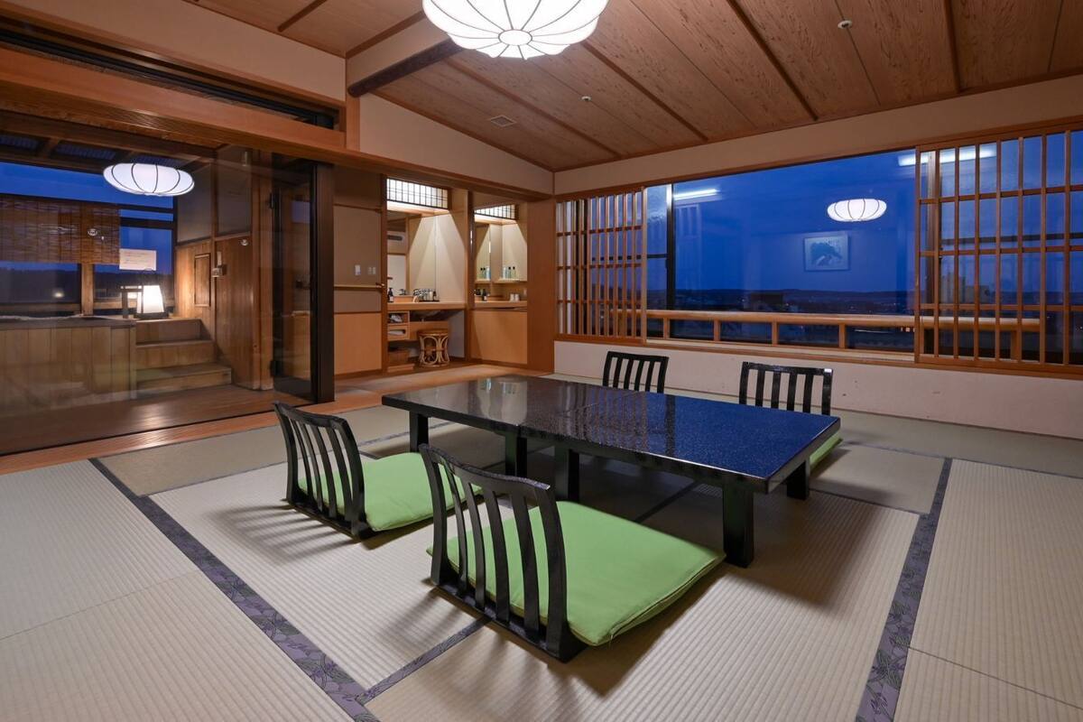 Una habitación con esteras tatami, una mesa baja y sillas, puertas correderas de madera y vistas a través de un mampara shoji.