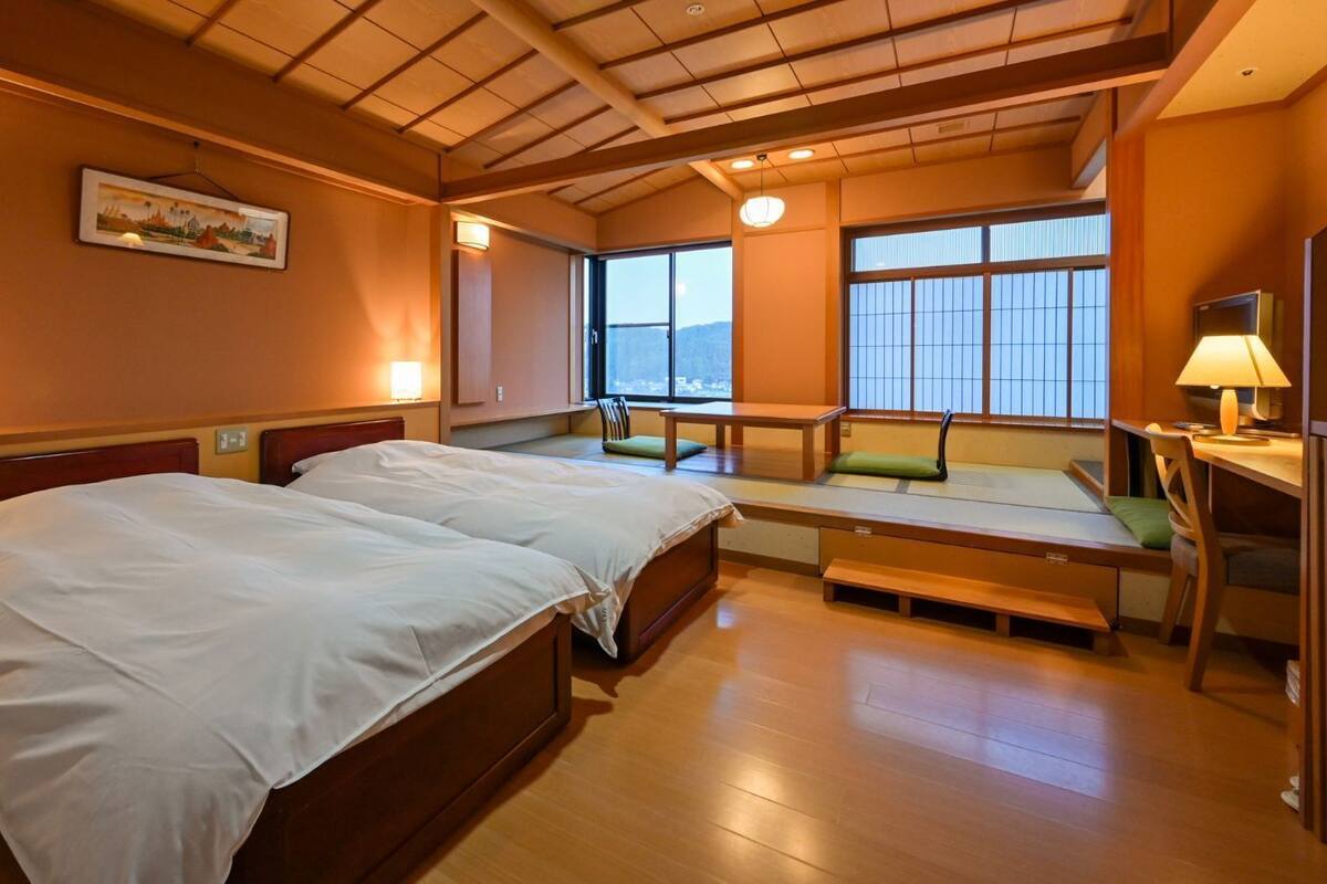 Habitación de hotel con dos camas, una zona de estar pequeña y vistas al exterior.