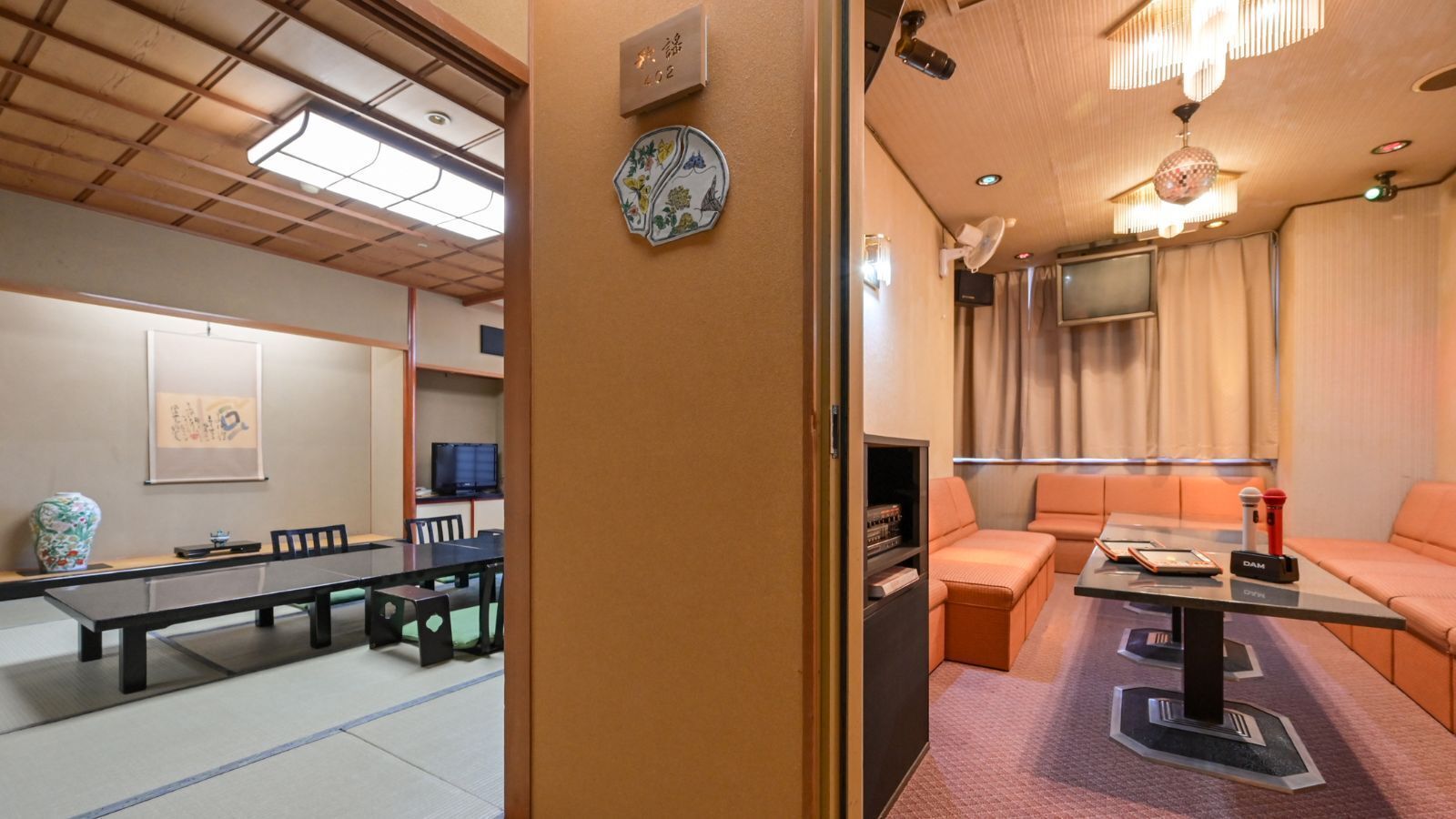 A hotel room with a tatami mat dining area, a sofa, a television, and a small cabinet.