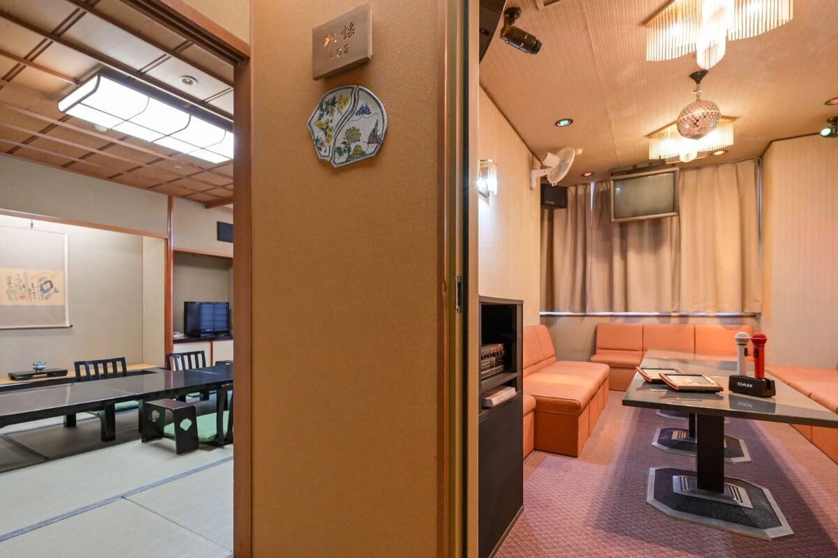 Habitación de hotel con zona de comedor con suelo de tatami, un sofá, un televisor y un pequeño armario.