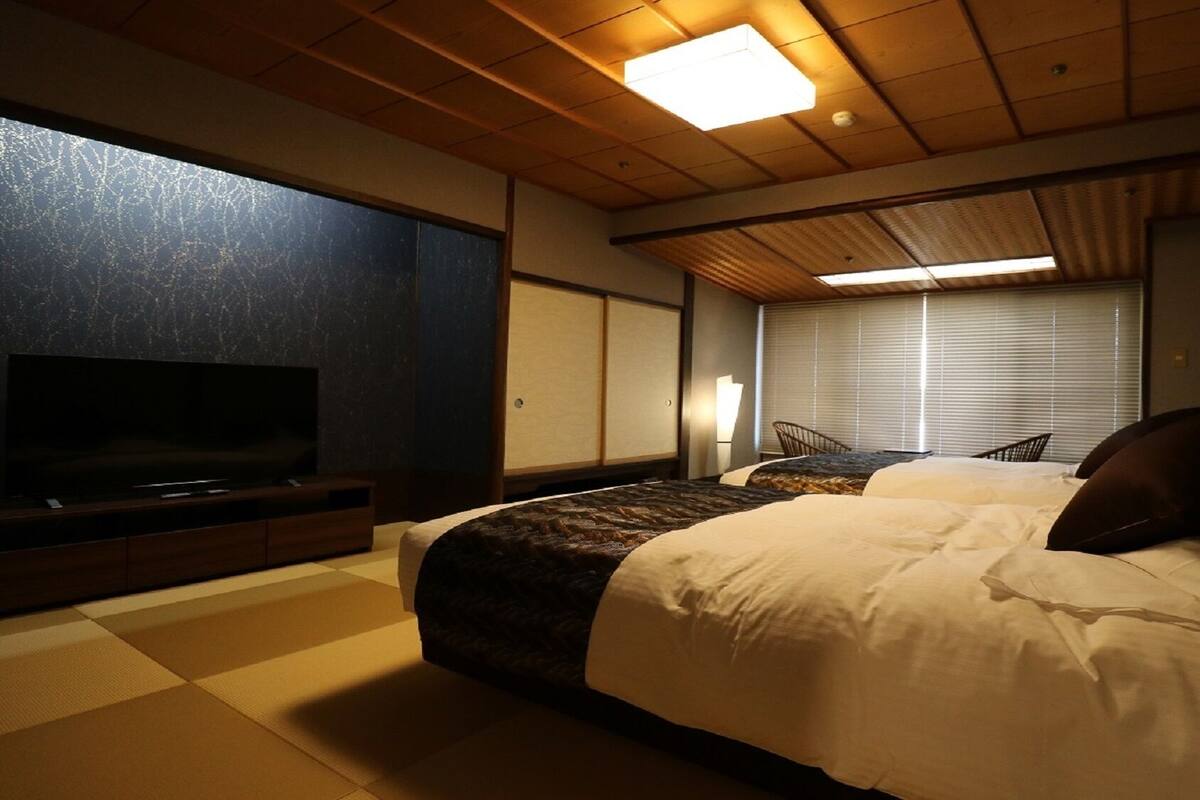 Una habitación de hotel con una cama grande, televisión, ventana con persianas y techo de madera.