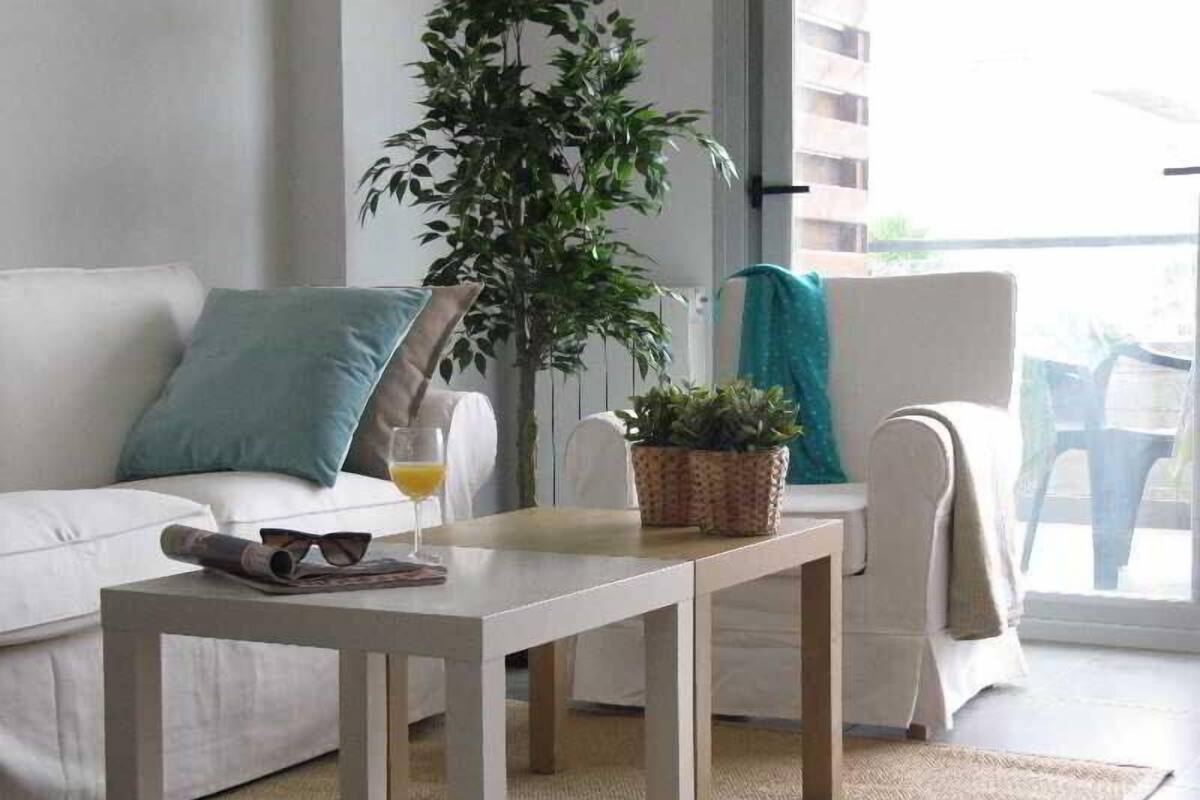 A modern living room with a white sofa, a small wooden table, a potted plant, and a glass of orange juice.