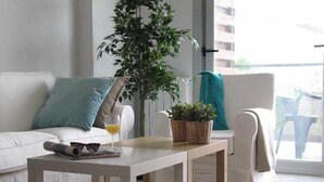 A modern living room with a white sofa, a small wooden table, a potted plant, and a glass of orange juice.