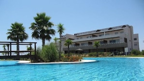 A hotel with a swimming pool, palm trees, and a modern building with balconies.