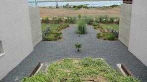 A courtyard with a gravel path, surrounded by plants and a view of the sea.