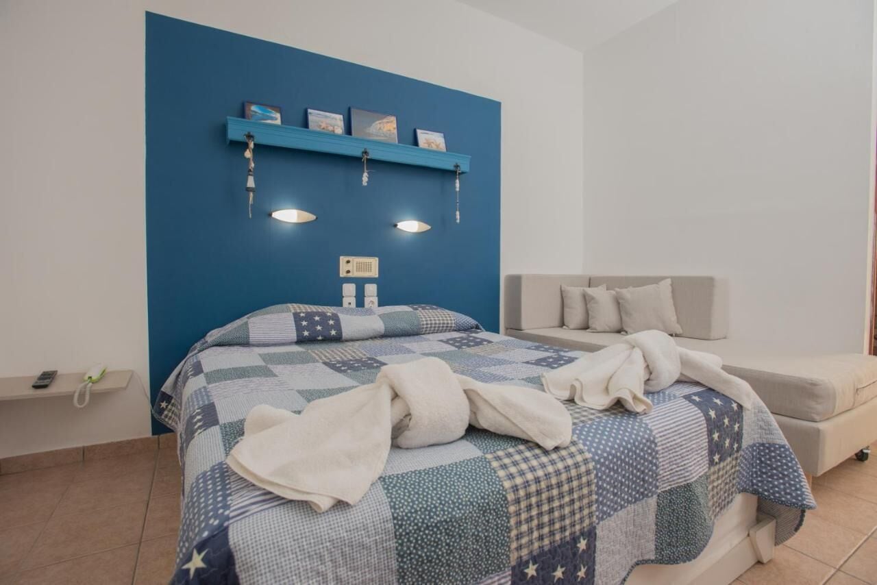 A bedroom with a blue accent wall, a bed with a quilt, a bedside table with a phone, and a sofa.