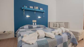A bedroom with a blue accent wall, a bed with a quilt, a bedside table with a phone, and a sofa.