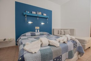 Quarto com parede azul de destaque, cama com colcha, mesa de cabeceira com telefone e um sofá.