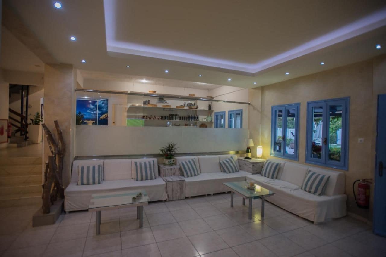 A modern living room with a sofa set, a coffee table, and a kitchen area with shelves and a window.