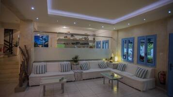 A modern living room with a sofa set, a coffee table, and a kitchen area with shelves and a window.