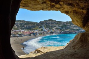 Uma vila costeira com edifícios ao longo da praia, vista através da entrada de uma caverna.