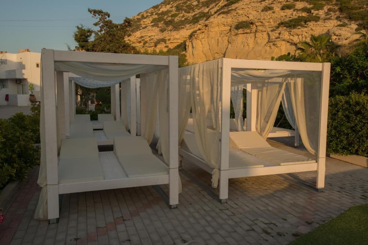 Two white, open-air beds with draped fabric, set on a paved area with a mountainous backdrop.