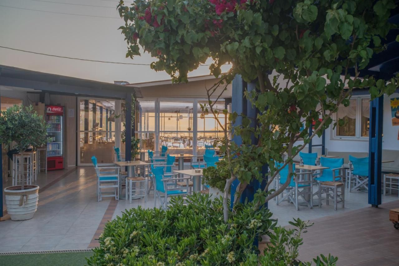 An outdoor seating area with tables and chairs, a Coca-Cola refrigerator, and a view of the beach through large windows.