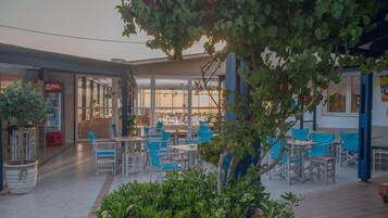 An outdoor seating area with tables and chairs, a Coca-Cola refrigerator, and a view of the beach through large windows.