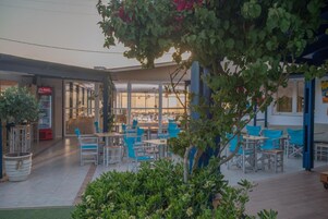 An outdoor seating area with tables and chairs, a Coca-Cola refrigerator, and a view of the beach through large windows.