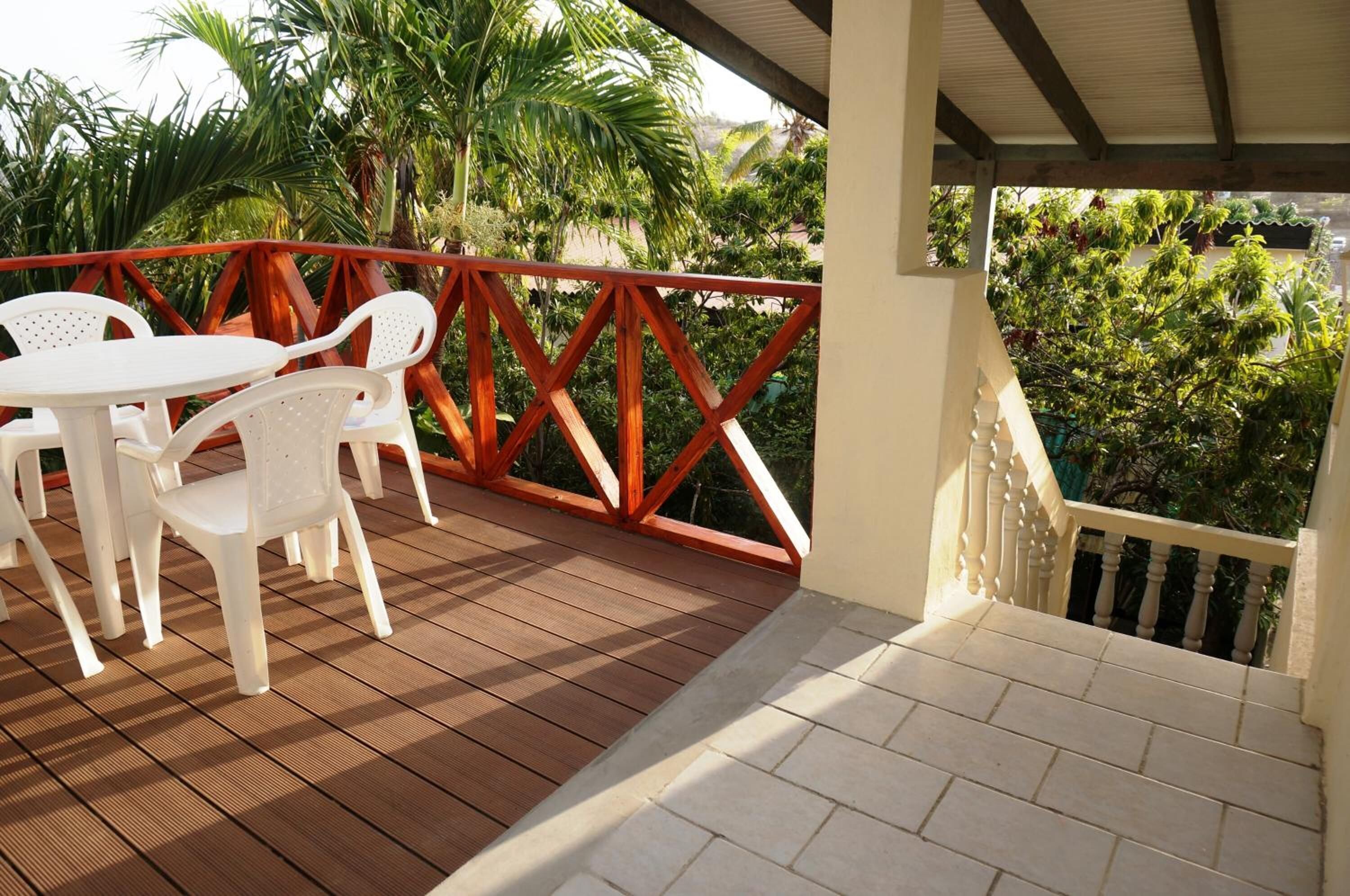 Un espacio al aire libre cubierto con piso de madera, sillas de plástico blanco y barandal rojo.