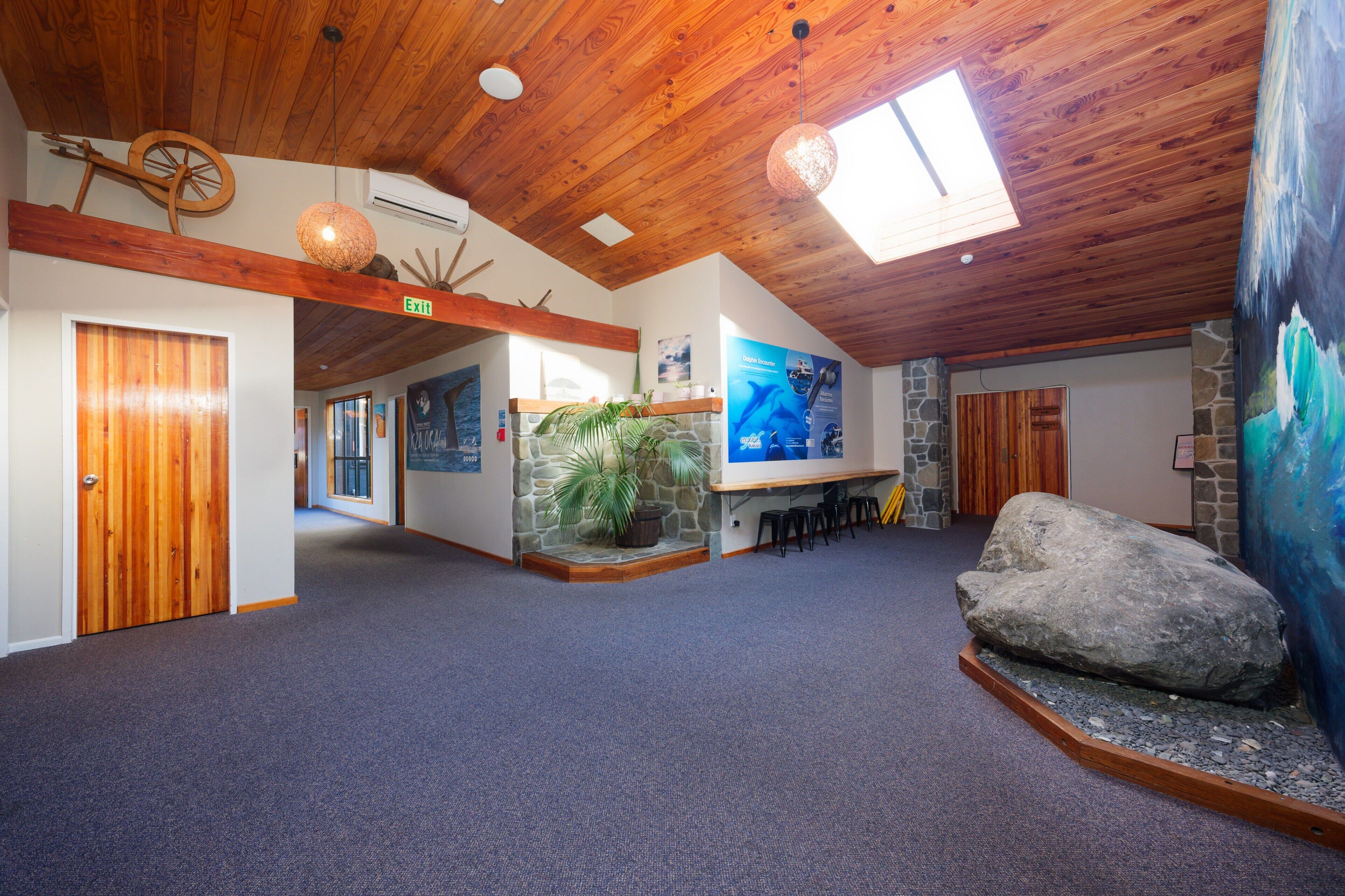 A spacious lobby with a high wooden ceiling, a stone wall, and a large rock feature.