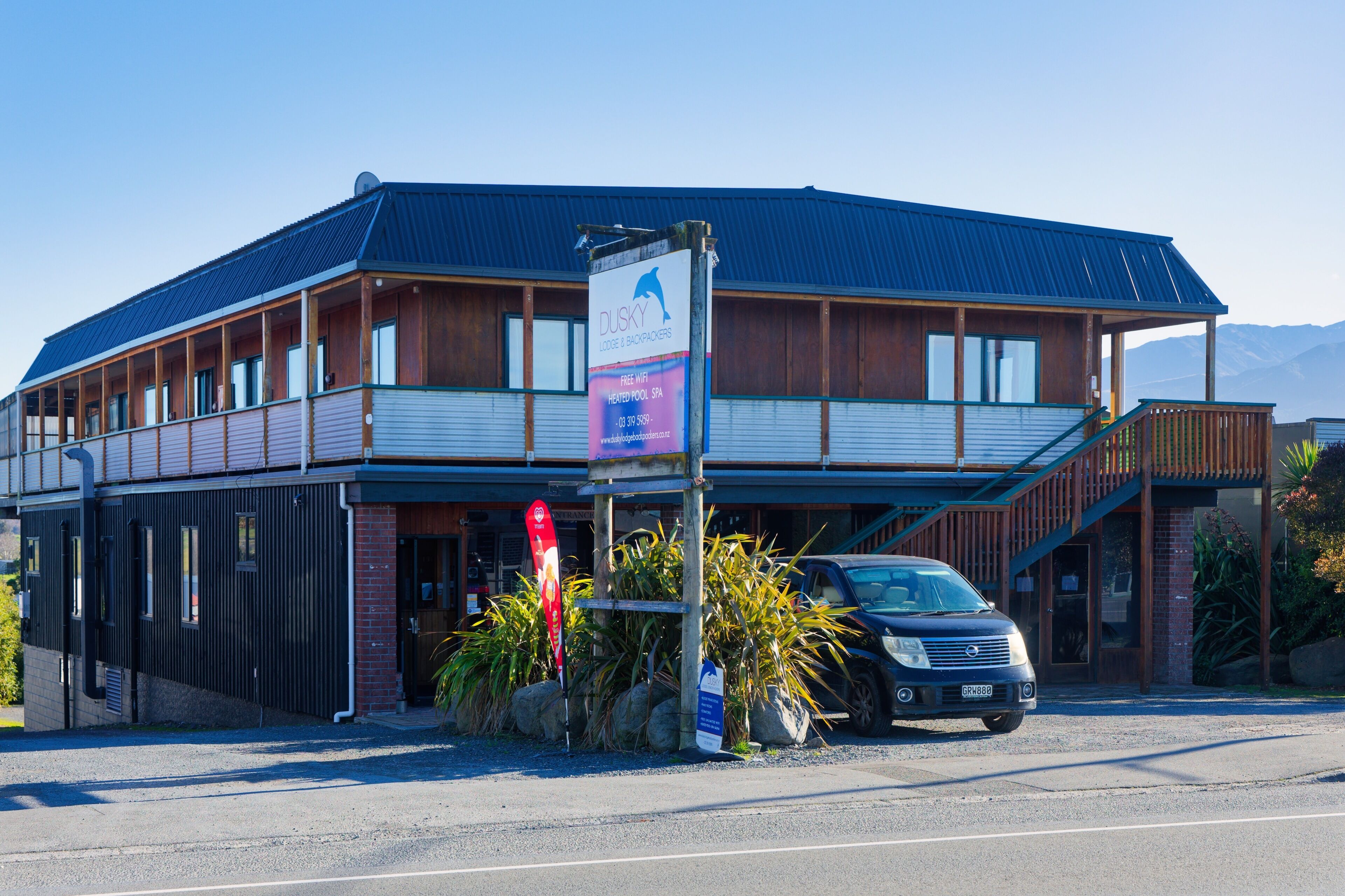 A two-story building with a blue roof, a signboard advertising a heated pool and spa, and a parked car in front.