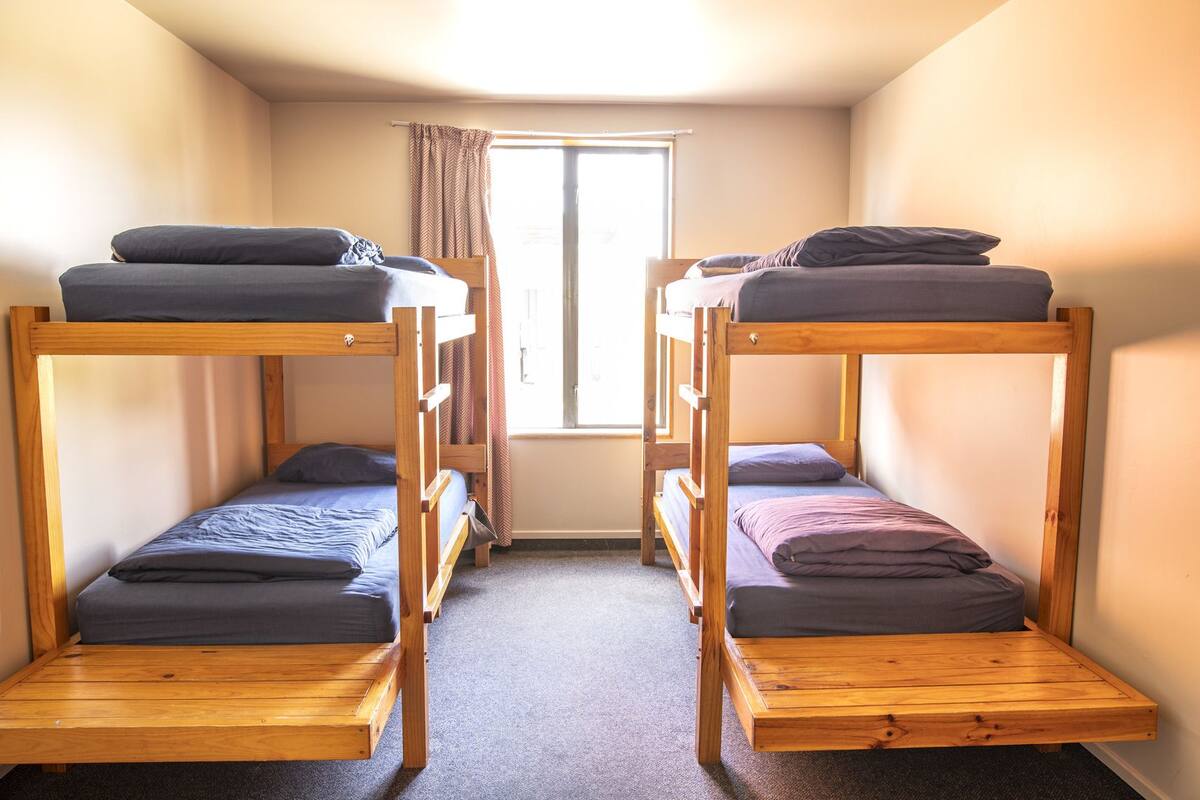 A room with two bunk beds, a window with curtains, and a carpeted floor.