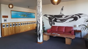 A reception area with a wooden bench, a red sofa, a wall mural of a whale, a framed picture of a coastal landscape, and a row of framed certificates. - Dusky Lodge - Hostel (Kaikoura)