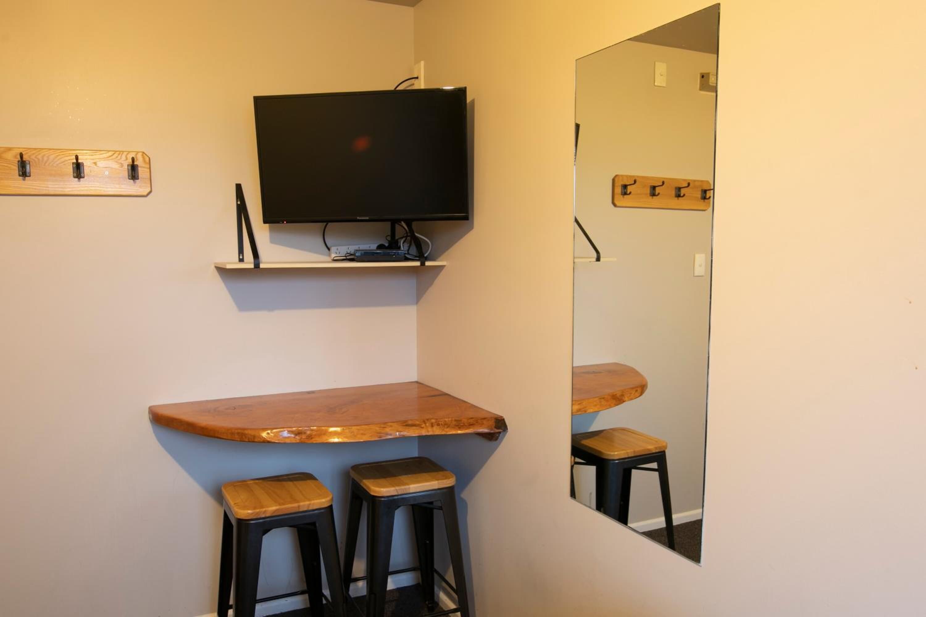 Eine kleine Bar mit Fernseher über einer Holztresen und drei Barhocker.