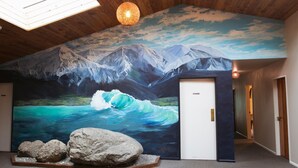 A room with a mural of a mountain landscape and a wave, a skylight, and a door. - Dusky Lodge - Hostel (Kaikoura)