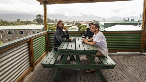 A wooden deck with a picnic table where three people are seated. - Dusky Lodge - Hostel (Kaikoura)
