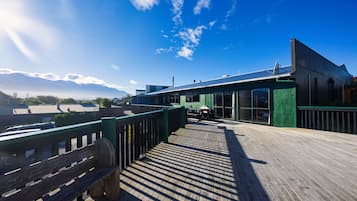 Una terraza de madera con un banco, un edificio de fachada verde y un cielo despejado.