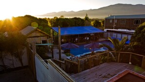 A pool area with umbrellas, a wooden deck, and a view of mountains. - Dusky Lodge - Hostel (Kaikoura)