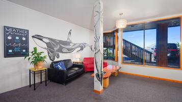 A modern interior with a large wall mural, a black leather sofa, a red chair, a wooden table, and a large window with a view of the outside.
