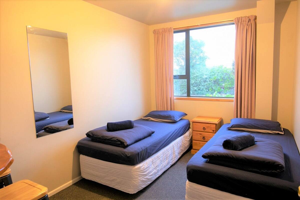 A bedroom with two beds, a wooden nightstand, a mirror, and a window with curtains.