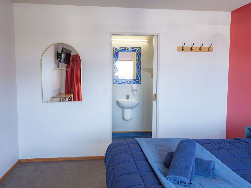 A bedroom with a bed, a mirror, a sink, and a door leading to another room.