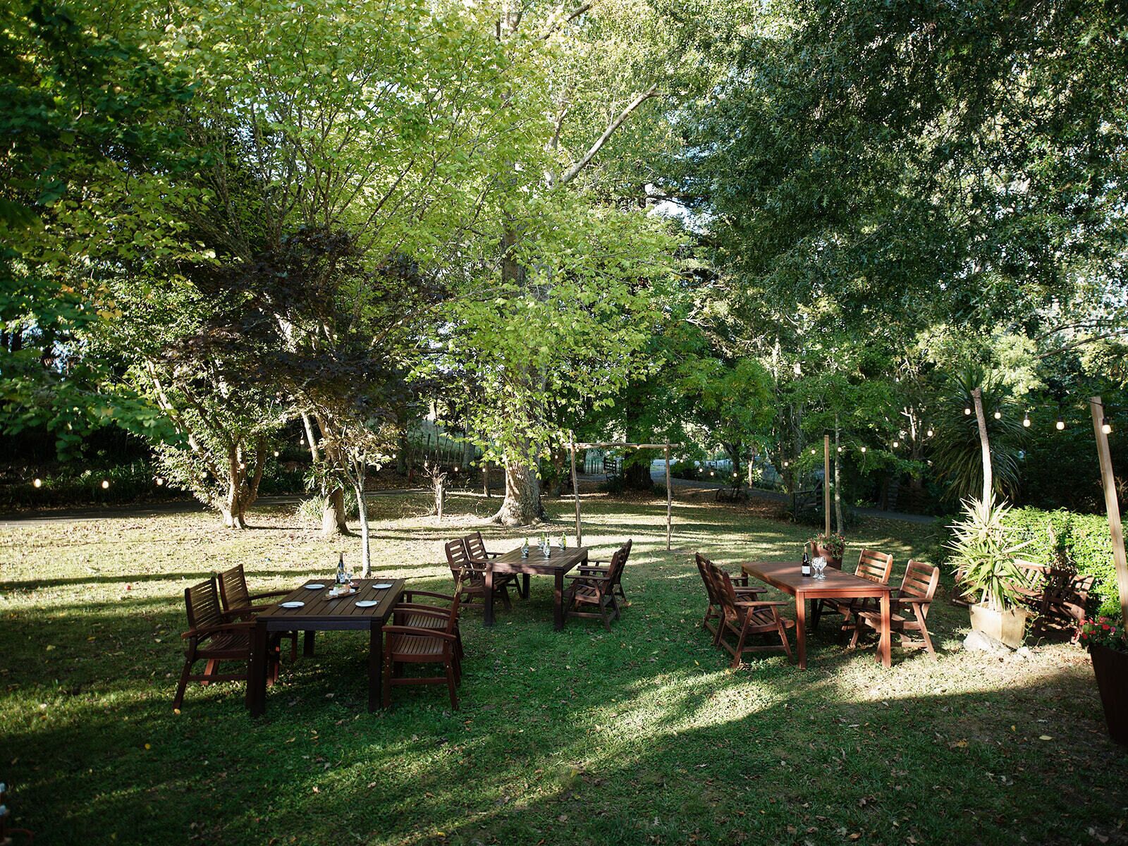 An outdoor dining area with wooden tables and chairs, surrounded by trees.