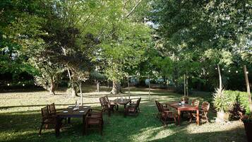 An outdoor dining area with wooden tables and chairs, surrounded by trees.