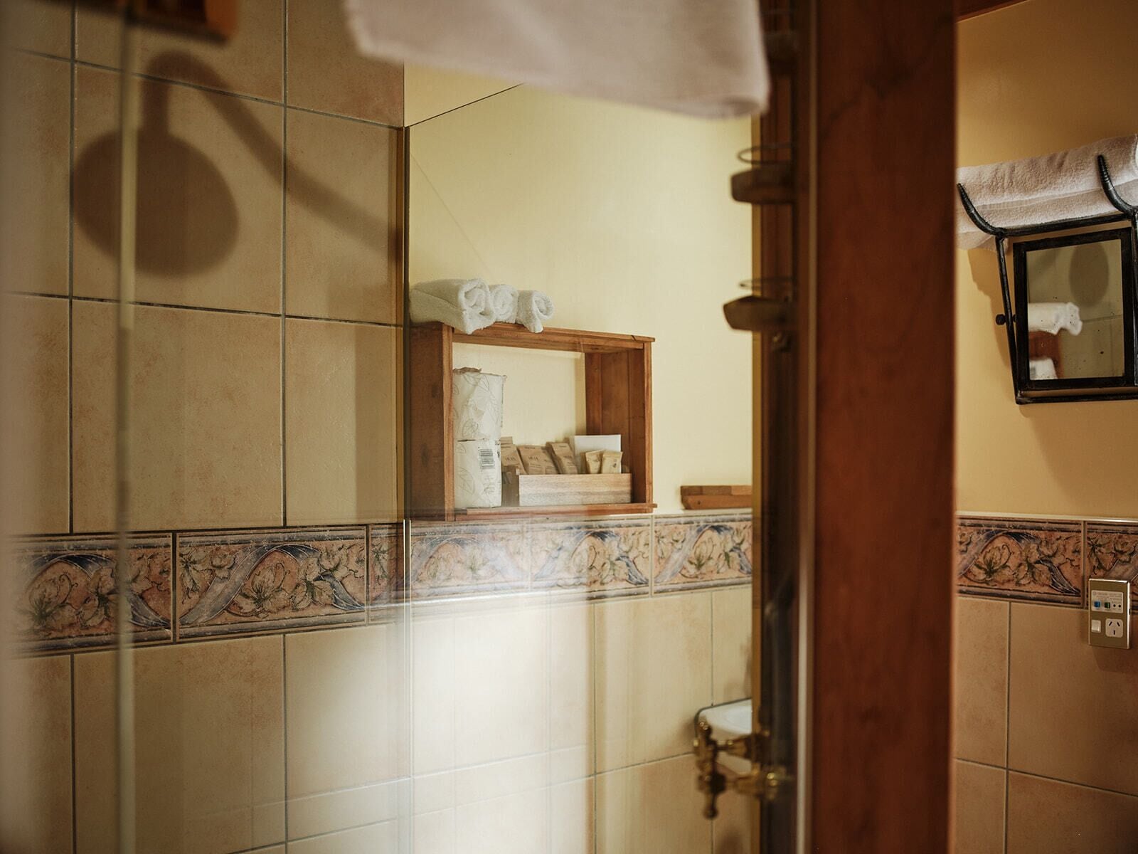 A bathroom with tiled walls, a wooden shelf with toiletries, a mirror, and a towel rack.