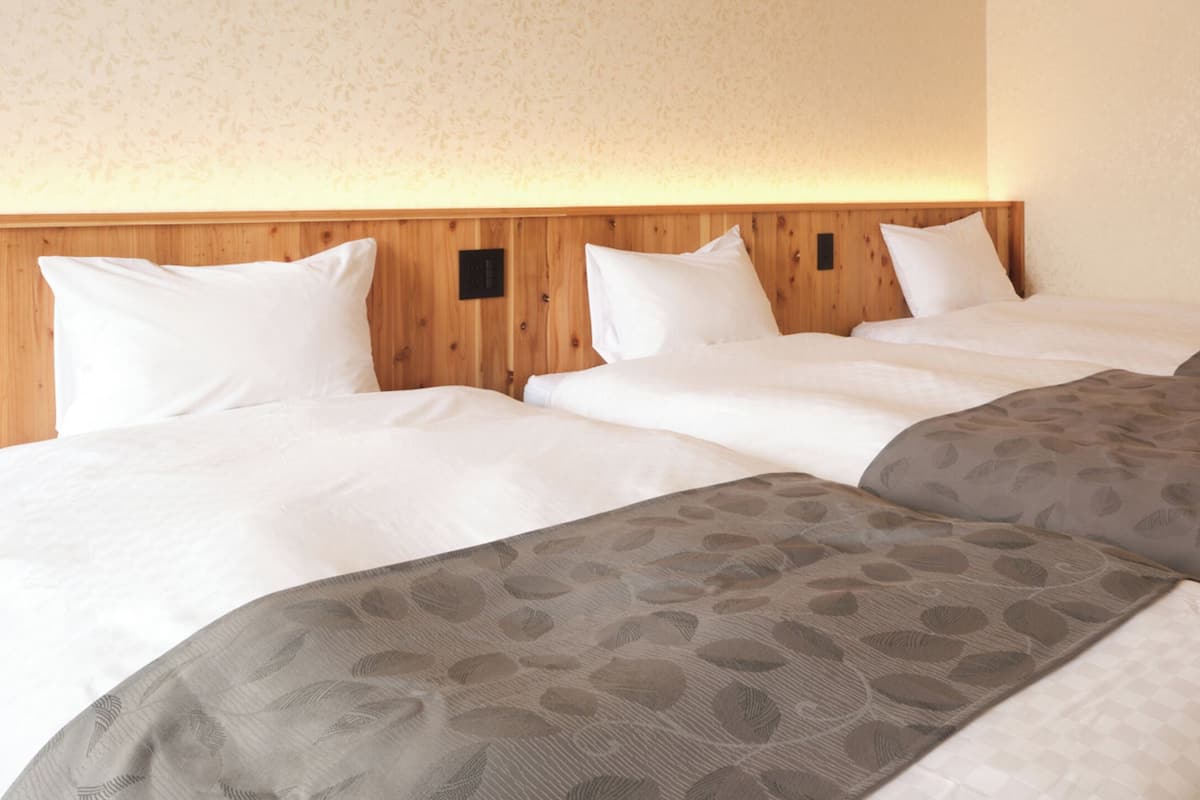 Une chambre d’hôtel avec une tête de lit en bois, deux lits avec une literie blanche et à motifs, et un mur à texture.