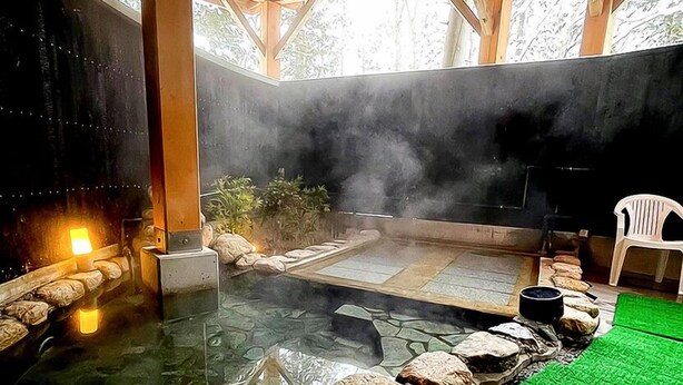 Un espace de sources chaudes doté d’un sol en pierre, de poutres en bois et d’une chaise en plastique blanche.