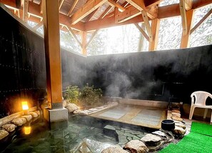 Un área de aguas termales con suelo de piedra, vigas de madera y una silla de plástico blanco.