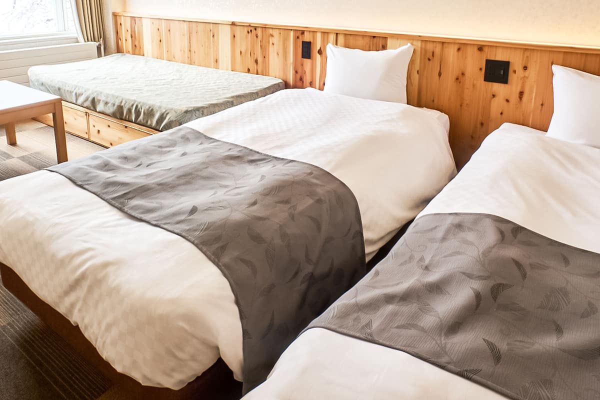 Une chambre d’hôtel avec deux lits simples, une tête de lit en bois, une petite table et une fenêtre avec des rideaux.