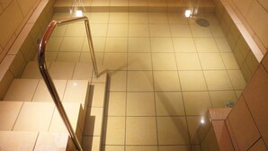 Un espace autour de la piscine revêtu de carrelage, avec une rambarde métallique et des marches menant à la piscine.
